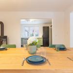 Esstisch mit blauen Tellern und grünen Stühlen. Im Hintergrund Küche und Kamin.