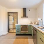 Küche mit grünen Schränken, Edelstahlgeräten und Fenster mit Blick auf Backsteinmauer.