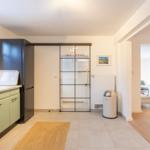 Küche mit grünen Schränken und schwarzer Kühlschranktür. Durchgang zur Wohnfläche mit Holzboden.