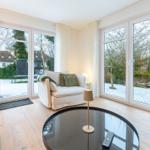 Wohnzimmer mit großem Fenster und Sitzgelegenheiten. Draußen Schnee und Garten.