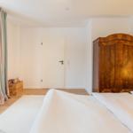 Schlafzimmer mit Bett, Holzschrank und Fenster mit Vorhängen.