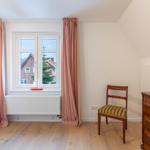 Schlafzimmer mit Fenster, Gardinen, Stuhl und Schrank.