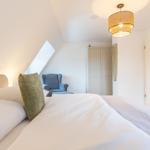 Schlafzimmer mit Dachschrägen, Bett, Sessel und Deckenlampe.