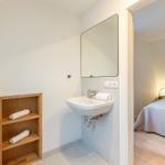 Badezimmer mit Waschbecken und Spiegel. Schlafzimmer mit Bett und Nachttisch sichtbar.