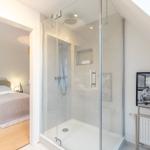 Duschbad mit Glaswand, Bett im Hintergrund, Wandbild und Heizkörper.