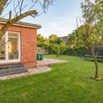 Rotes Backsteinhaus mit Terrasse und grünem Garten mit Trampolin.