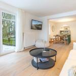 Wohnzimmer mit Sofa, Couchtisch und Fernseher. Durchgang zur Küche mit Esstisch und Kamin.