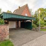 Haus mit Carport, Garagen- und Torbereich, umgeben von Grün und Steinmauern.
