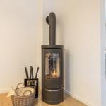 Kaminofen mit brennendem Feuer in einem Raum mit Holzboden und Blick in die Küche.