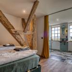 Schlafzimmer mit massivem Holzgestell und angrenzender Dusche mit Fenster.