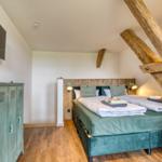 Schlafzimmer mit Doppelbett, Holzbalken und Fernseher an der Wand.
