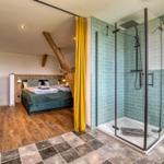 Schlafzimmer mit Doppelbett und Duschbad mit Glaswand und Fliesen.