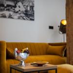 Gelber Sofa mit Obstschale auf Tisch, Holzpfosten und Wandbild im Hintergrund.