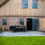 Haus mit Holz- und Ziegelwand, Terrasse mit Sitzgelegenheiten und Garten.