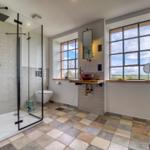 Badezimmer mit Dusche, Waschbecken und Fenstern mit Blick auf Landschaft.