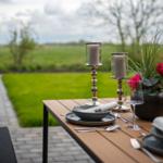 Garten-Tisch mit Teller, Besteck und Blumen. Hintergrund: Grasfläche und Weg.