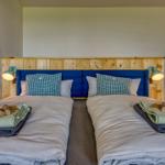 Zwei Betten mit blauem Kopfteil und Holzpaneelen an der Wand.