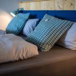 Bettkopfteil mit blauem Polster und Holzverkleidung, dekoriert mit Kissen und Bettwäsche.