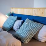 Bettkopfteil aus Holz und blauem Stoff mit Kissen und Nachttischlampe.