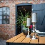 Außenbereich mit Holztisch, Kerzenhaltern und Pflanze vor Backsteinmauer