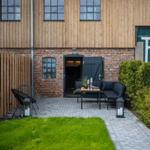 Hinterhof mit Sitzbereich, Grasfläche und Steinplattenweg vor Holz- und Ziegelhaus.