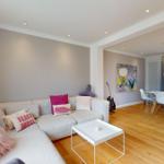 Wohn- und Essbereich mit Sofa, Tisch und Stühlen. Holzboden und Wandbild sichtbar.