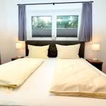 Schlafzimmer mit Doppelbett, zwei Nachttischen und Fenster mit Jalousien.