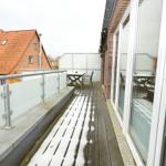 Terrasse mit Tisch und Stühlen, teilweise mit Schnee bedeckt, Blick auf ein Haus mit rotem Dach.