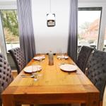 Esszimmer mit Holztisch und gepolsterten Stühlen. Durchgänge zu Balkon und Garten.