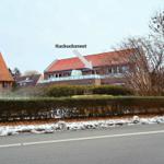 Haus mit rotem Dach und Balkon hinter Hecke