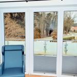 Ein blauer Sessel vor großen Fenstern mit Blick auf Balkon und Straße.