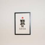 Ein gerahmtes Bild einer schwarzen Kuckucksuhr mit rotem Dach und dem Text Kuck Kuck.