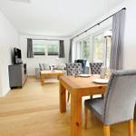 Esszimmer mit Holztisch und Stühlen. Wohnbereich mit Sofa und Fernseher.