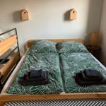 Zwei Betten mit grün-weißem Bettzeug und gefalteten Handtüchern. Wanddekoration mit Holzhausfiguren.