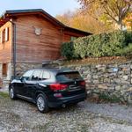 Holzhaus mit Steinmauer und gepflastertem Hof. Ein schwarzes Auto steht vor dem Haus.