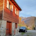 Holzhaus mit Steinbasis, schwarzes Auto auf Kiesweg, Berge im Hintergrund