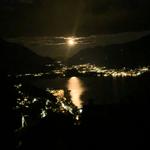 Nachtansicht über einen See mit Mond und beleuchteten Ortschaften