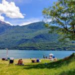 Grüner Strand mit Menschen, See und Bergen im Hintergrund.
