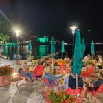 Nachtansicht eines Uferrestaurants mit Gästen, Tischen, Stühlen und grünen Sonnenschirmen.