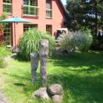 Rotes Haus mit grünen Fenstern, Garten mit Steinen und Sonnenschirm.