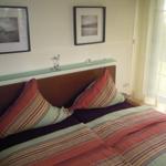 Schlafzimmer mit Bett, Wandbildern und Fenster mit Vorhängen.