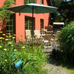 Terrasse mit Tisch, Stühlen und Sonnenschirm vor rotem Haus mit grünen Fenstern.
