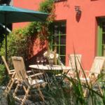 Terrasse mit Tisch, Stühlen und Sonnenschirm vor rotem Haus mit grünen Fenstern.