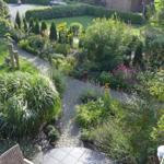 Garten mit Steinsäule, Blumenbeete und gepflastertem Weg von Balkon aus gesehen