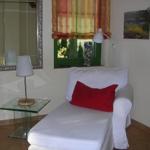 Weißes Sofa mit rotem Kissen, Glas-Tisch, Wandspiegel und Fenster mit Vorhang.