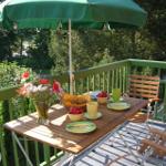 Terrasse mit Tisch, Stühlen und grünem Sonnenschirm. Frühstückstablett mit Obst und Blumen.