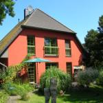 Rotes Haus mit grünen Fenstern und Garten unter blauem Himmel.