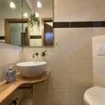 Bad mit Waschbecken, Spiegel und Toilette. Wandfliesen und Holzunterschrank.