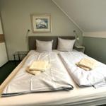 Schlafzimmer mit Doppelbett, Nachttischen und Wandbild unter Dachschrägen.