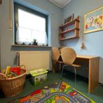 Ein Kinderzimmer mit Schreibtisch, Stühlen, Spielteppich und Bücherkorb.